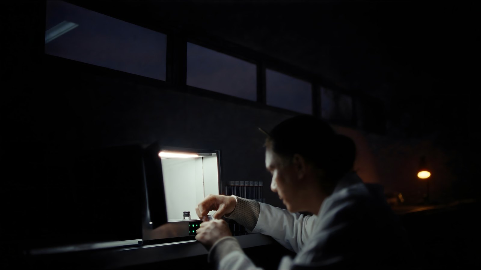 A researcher seats a small vial in a bench-top instrument in a dark laboratory, lit by the instrument's own lamp