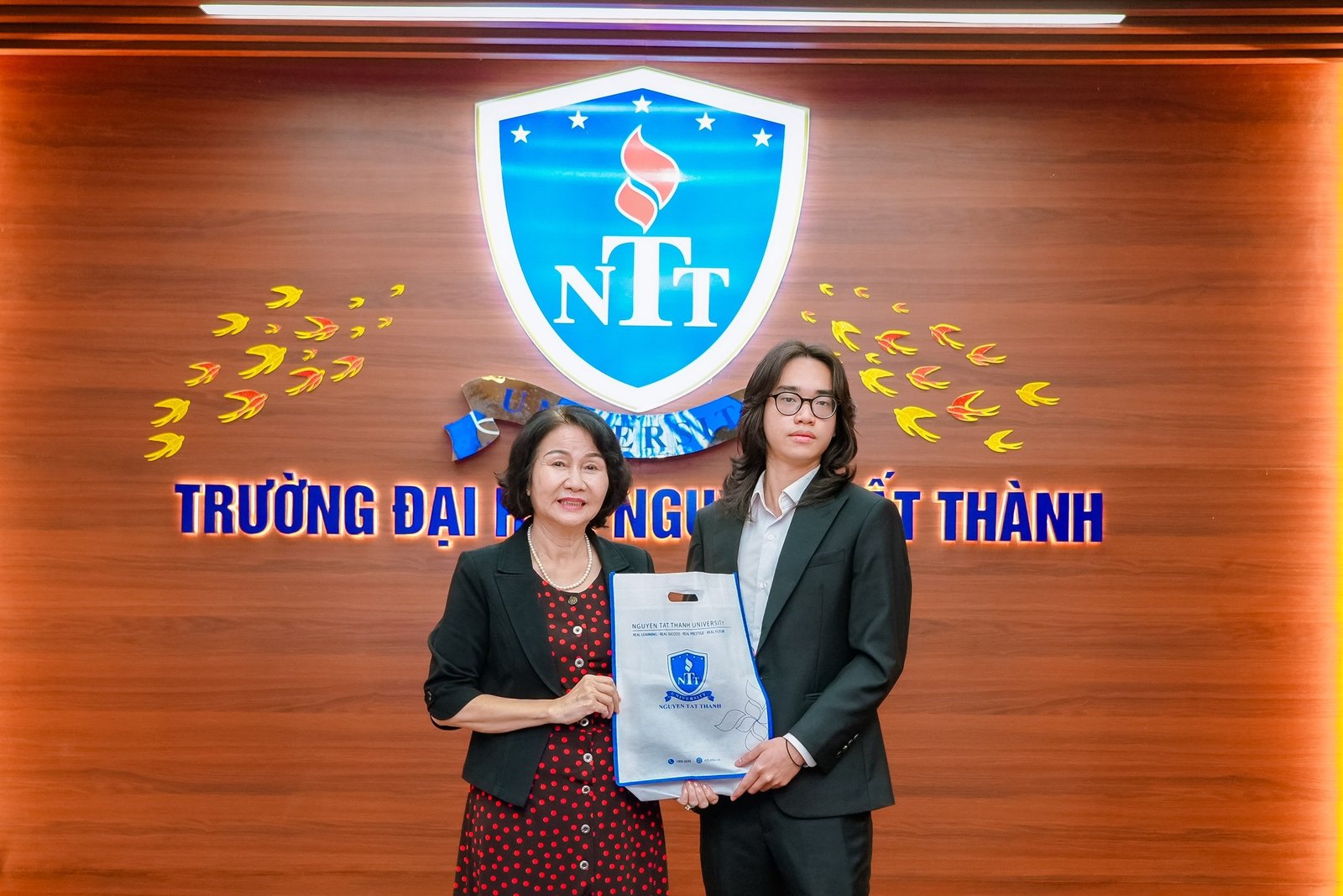 Two people holding the signed research agreement in front of the emblem of Nguyen Tat Thanh University