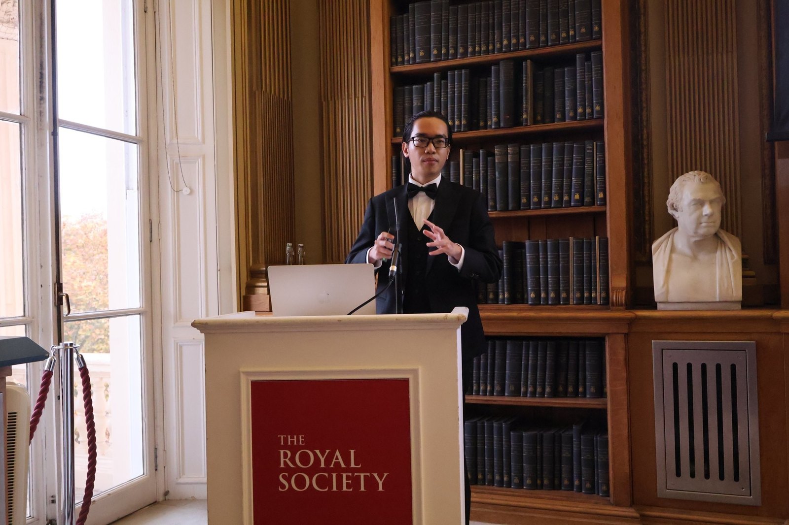 Marshon Nguyen speaking at a lectern in the library of the Royal Society in London